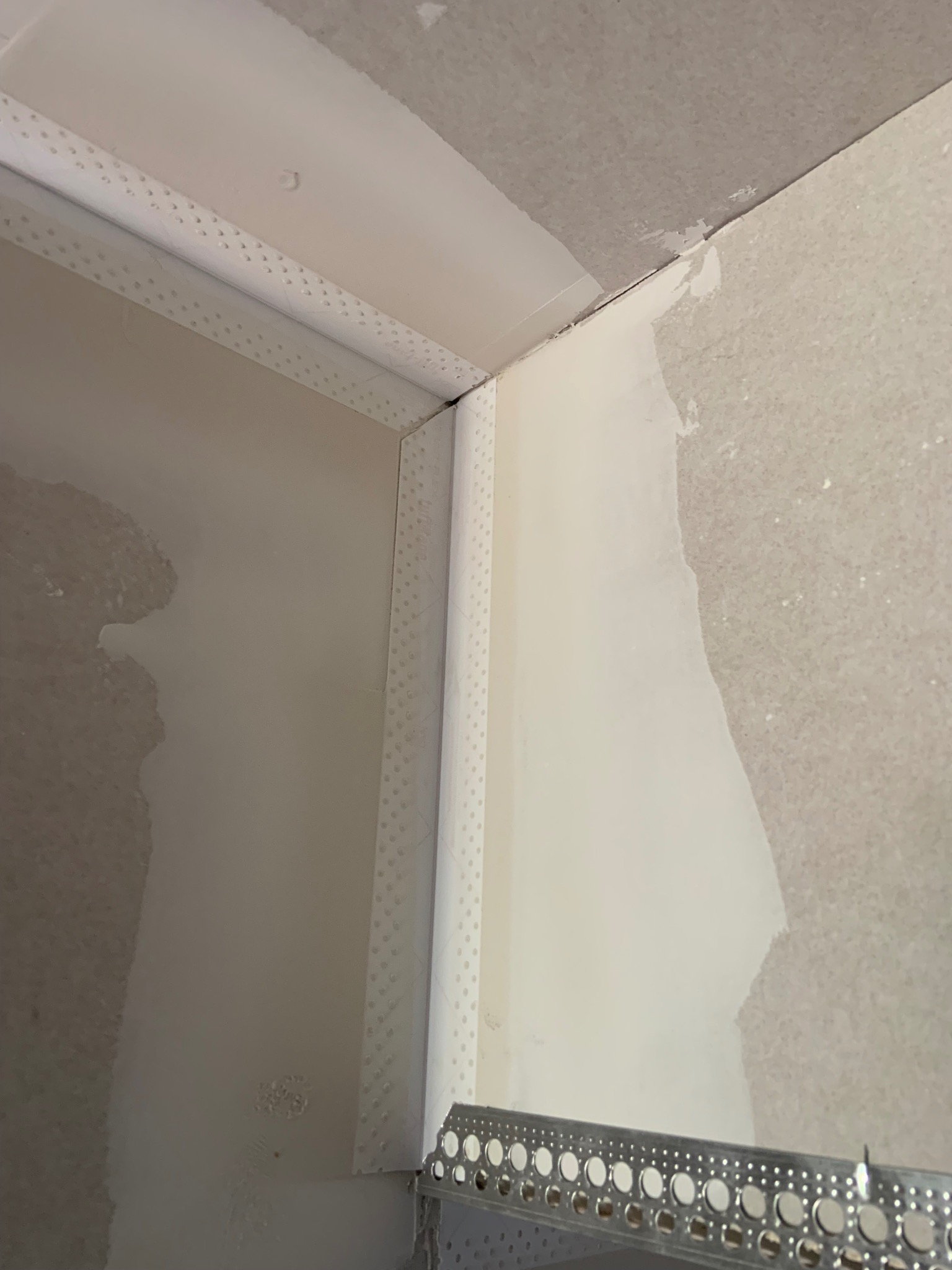 Przygotowanie narożnika ściany do szpachlowania z użyciem listwy narożnikowej w Bielawie. Widoczne ślady szpachli na ścianie i suficie.