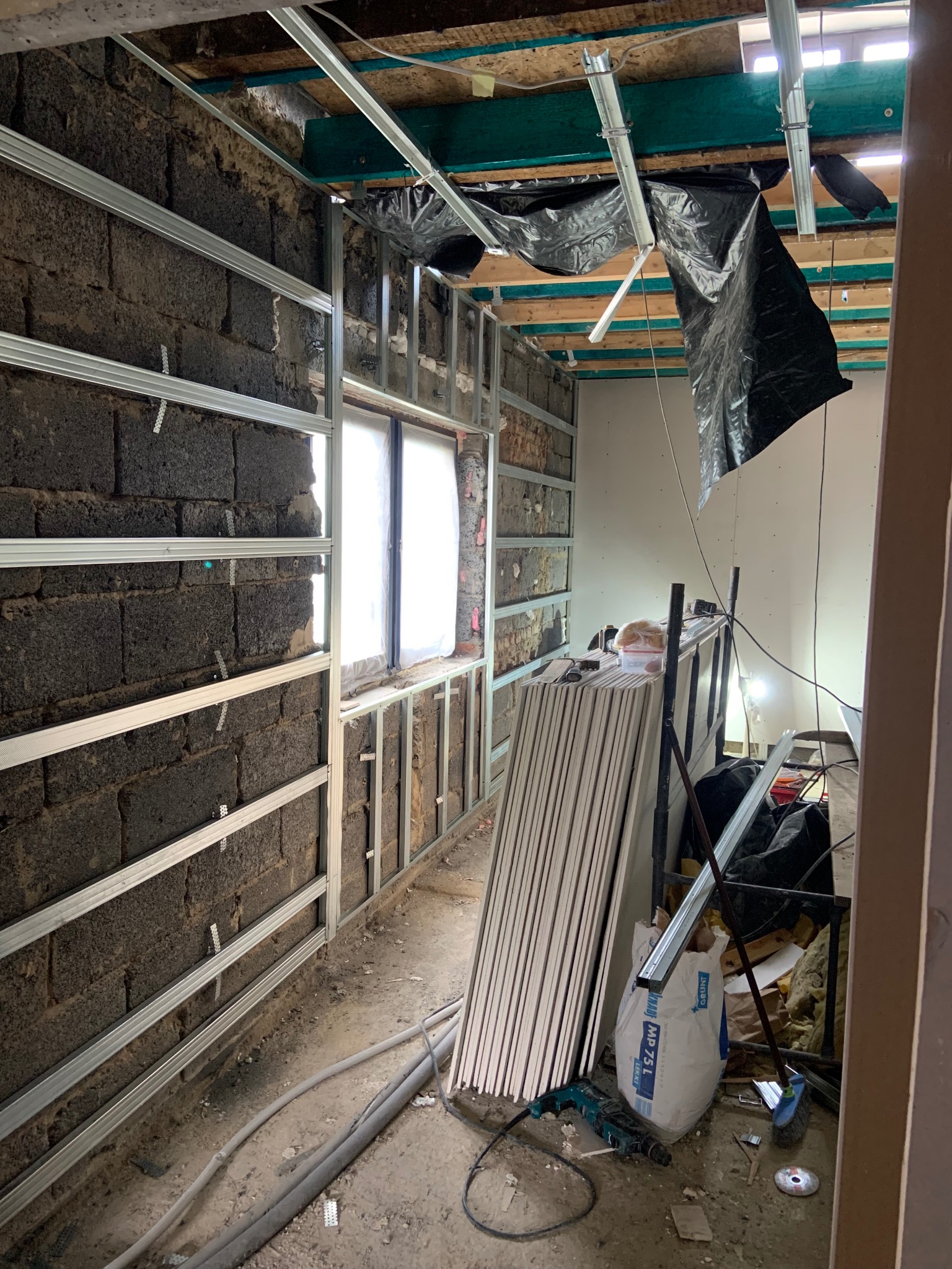 Montaż stelaża pod płyty gipsowe na ścianach z pustaków. Widoczne profile, płyty, narzędzia i worki z zaprawą. Przygotowanie do wykończenia wnętrza.