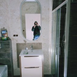 Tomasz koczorowski - Wykończona łazienka z beżowymi płytkami imitującymi marmur, kabiną prysznicową i umywalką z szafką. W lustrze odbija się osoba robiąca zdjęcie.