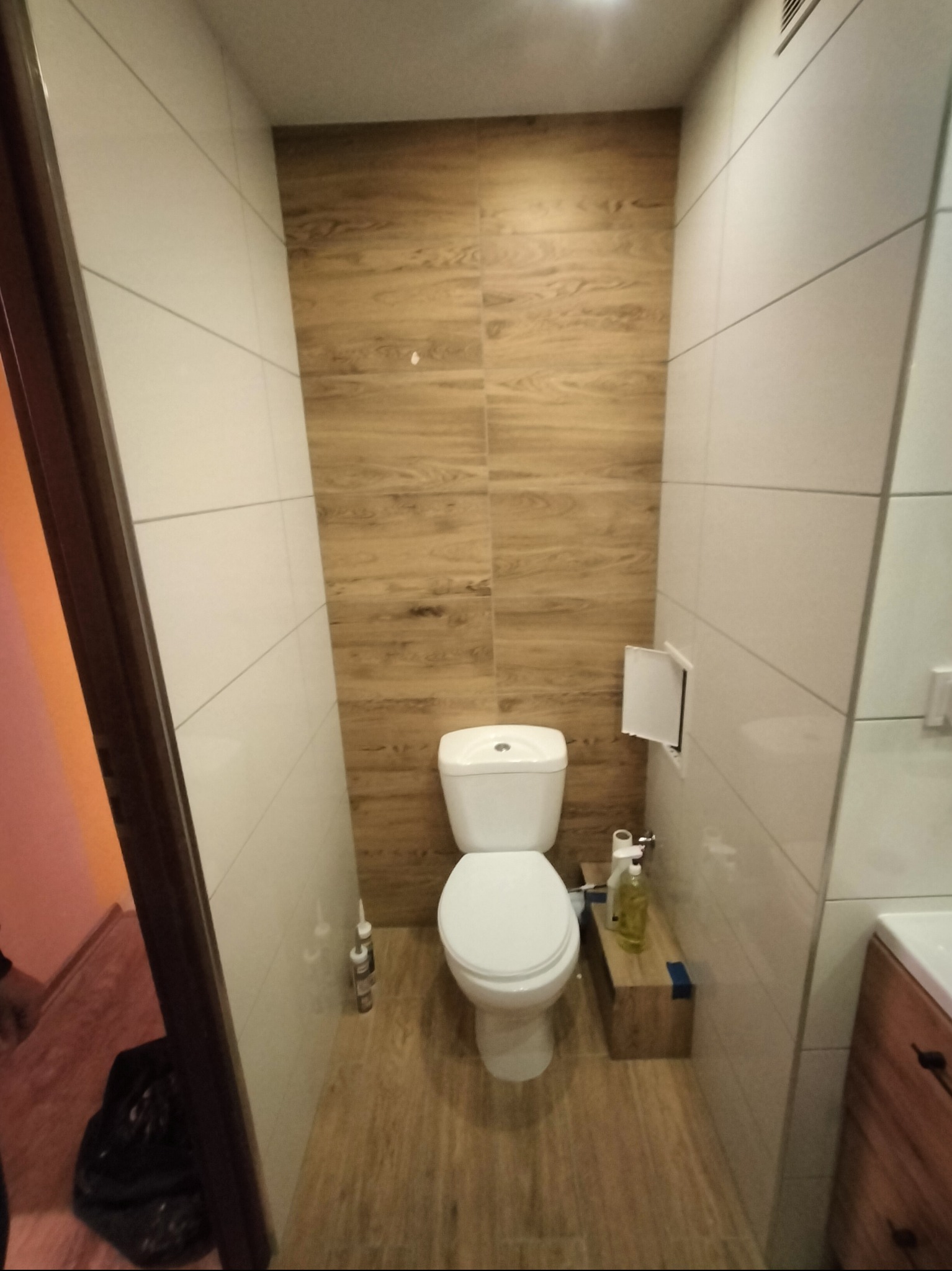 Nowoczesna toaleta z drewnopodobnymi płytkami na ścianie akcentowej i podłodze. Biała ceramika sanitarna, minimalistyczny design, oświetlenie górne. Wykończona łazienka.