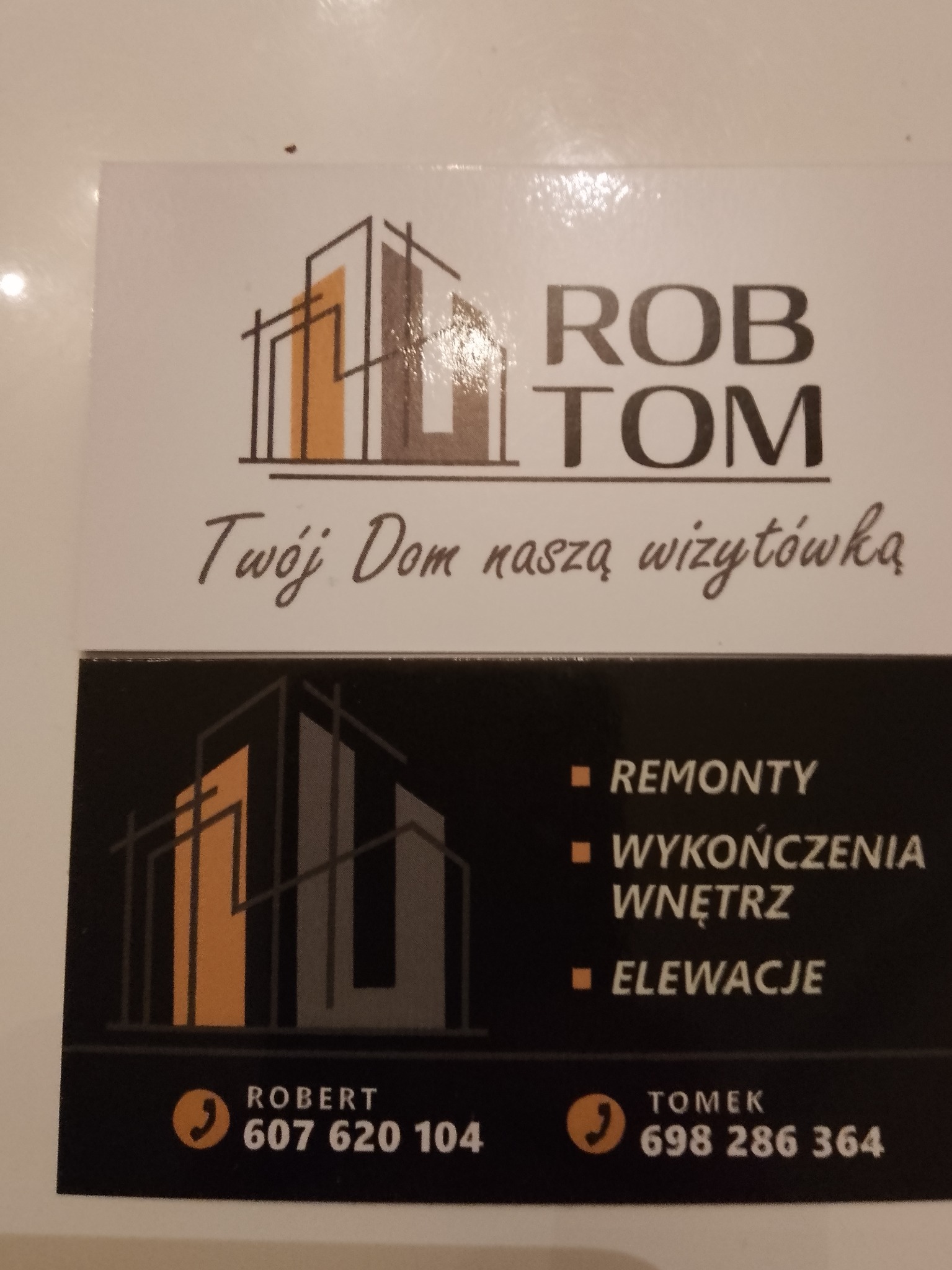 Wizytówka firmy budowlanej Rob-Tom z logo przedstawiającym budynek. Oferta obejmuje remonty, wykończenia wnętrz i elewacje. Numery kontaktowe do Roberta i Tomka.