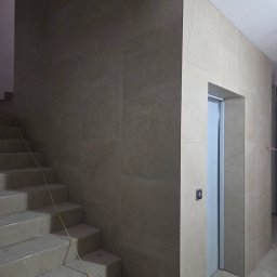 ArtBud - Wykończone płytkami schody i ściany w Szczecinie. Widoczne stopnie schodów, ściana wyłożona płytkami oraz wejście do pomieszczenia z zamontowanymi drzwiami.