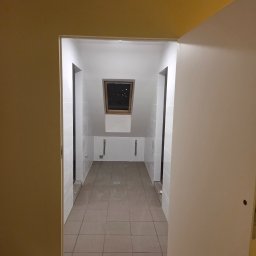 ArtBud - Wykończona łazienka na poddaszu w Szczecinie. Ułożone płytki podłogowe i ścienne, widoczne rury. Ujęcie z korytarza przez otwarte drzwi.