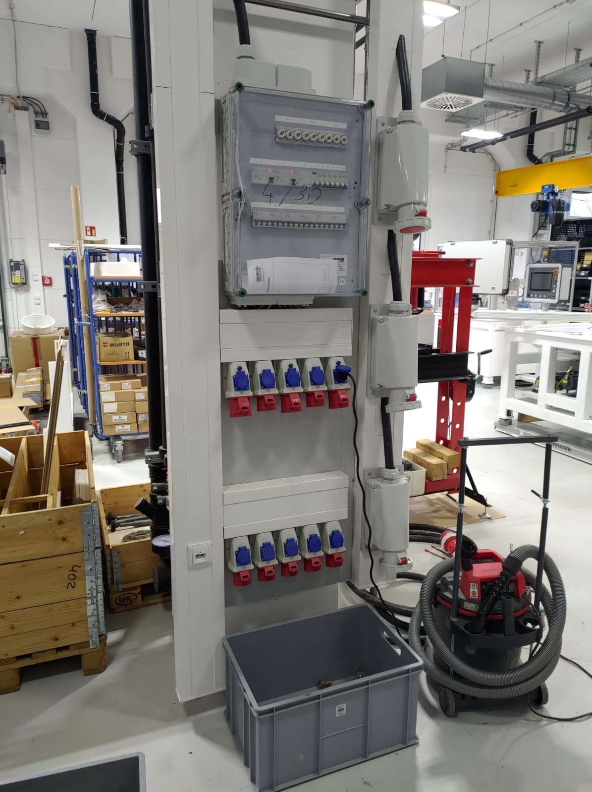 Rozdzielnica elektryczna z gniazdami siłowymi w Tuchowie. Widoczne zabezpieczenia, gniazda z wtyczkami i skrzynka z bezpiecznikami. Obok odkurzacz przemysłowy.
