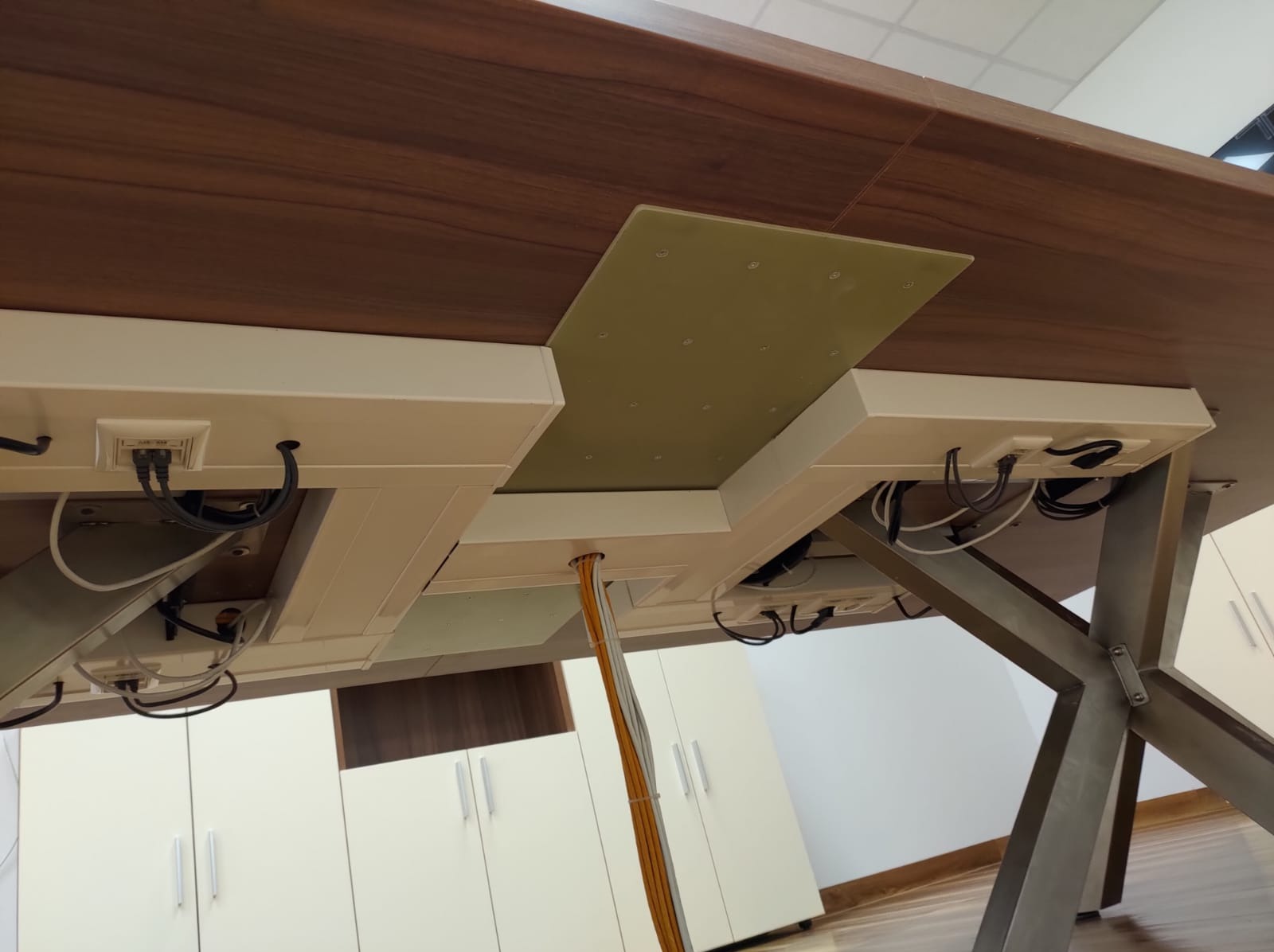 Spód biurka z zamontowanymi gniazdkami i kablami, widok z dołu, ukazujący estetyczne prowadzenie przewodów w biurze.