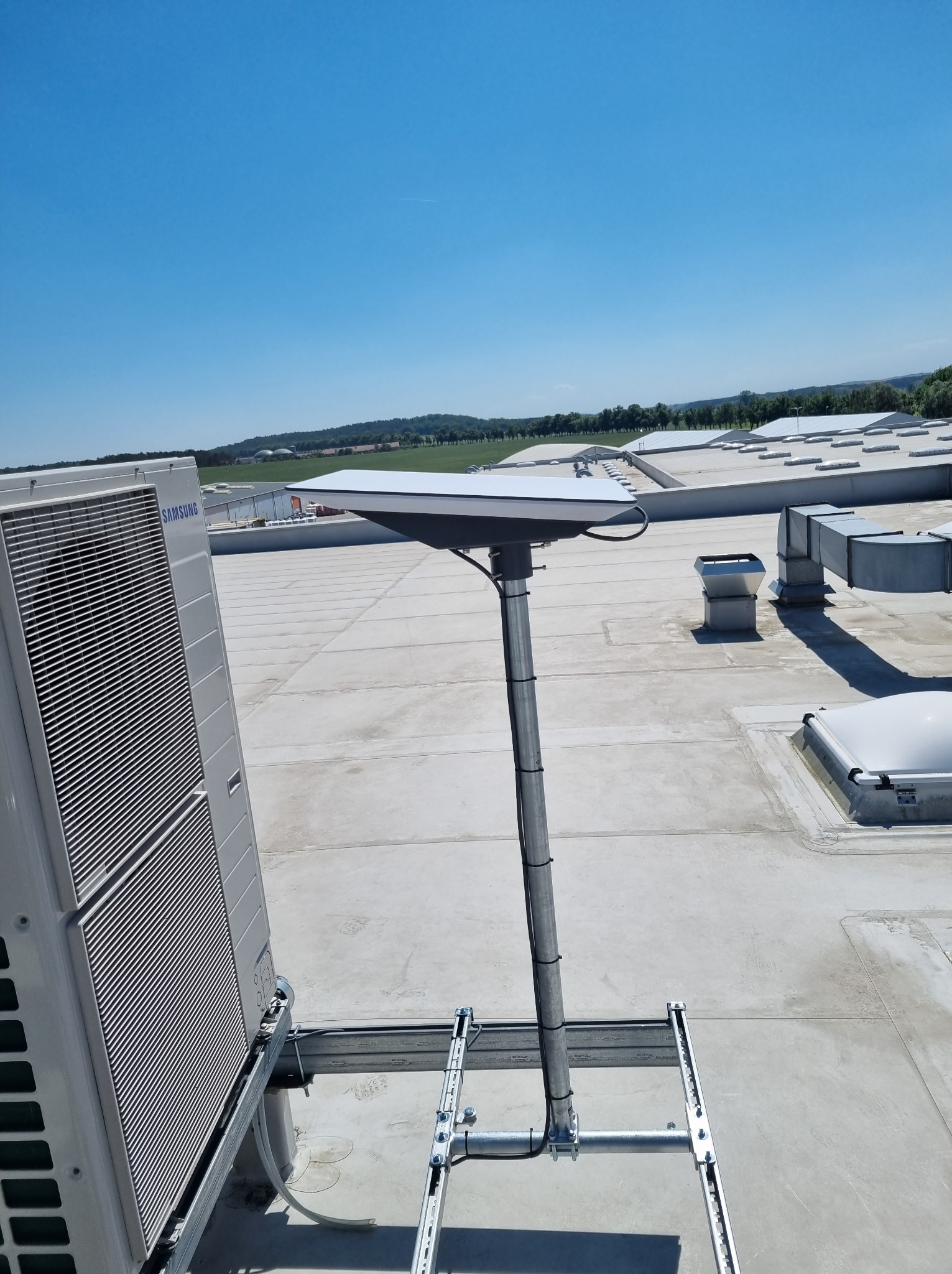 Antena internetowa na dachu budynku z klimatyzatorem Samsung, widok z góry w słoneczny dzień. Instalacja anteny na metalowej konstrukcji.