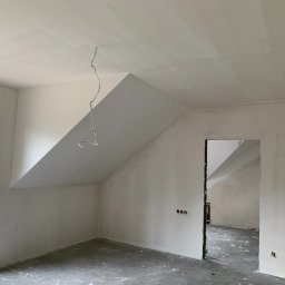 OLEH PYLYPCHAK - Pokój na poddaszu w trakcie prac wykończeniowych: ściany i sufit pokryte gładzią, widoczne kable, okno z widokiem na zieleń, surowy beton na podłodze.