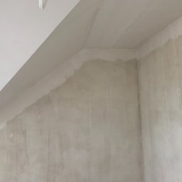 OLEH PYLYPCHAK - Ściana po nałożeniu gładzi szpachlowej, widoczne nierówności i przygotowanie do dalszych prac wykończeniowych. Ujęcie z dołu, fragment sufitu.