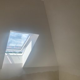 OLEH PYLYPCHAK - Białe, świeżo pomalowane poddasze z oknem dachowym, przez które widać błękitne niebo. Dolna część ściany przygotowana do dalszych prac wykończeniowych.