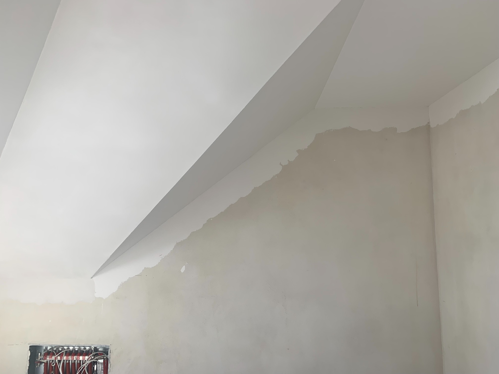 Skośny sufit po gładzi, częściowo pomalowany na biało, z widoczną instalacją grzewczą w ścianie. Ściana w trakcie prac wykończeniowych.