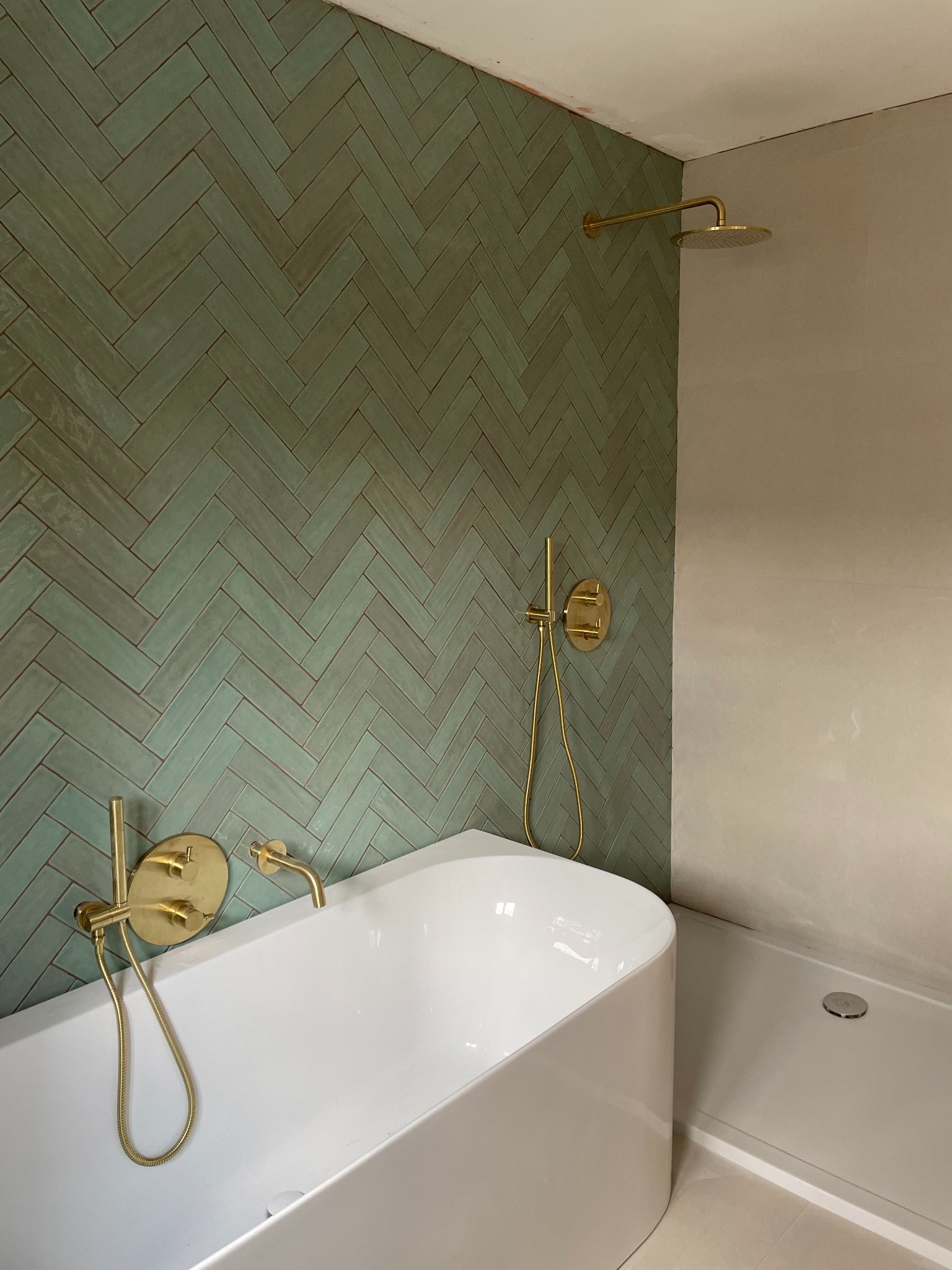 Nowoczesna łazienka z zieloną, ułożoną w jodełkę glazurą, złotą armaturą i białą wanną oraz brodzikiem. Minimalistyczny design, eleganckie wykończenie.