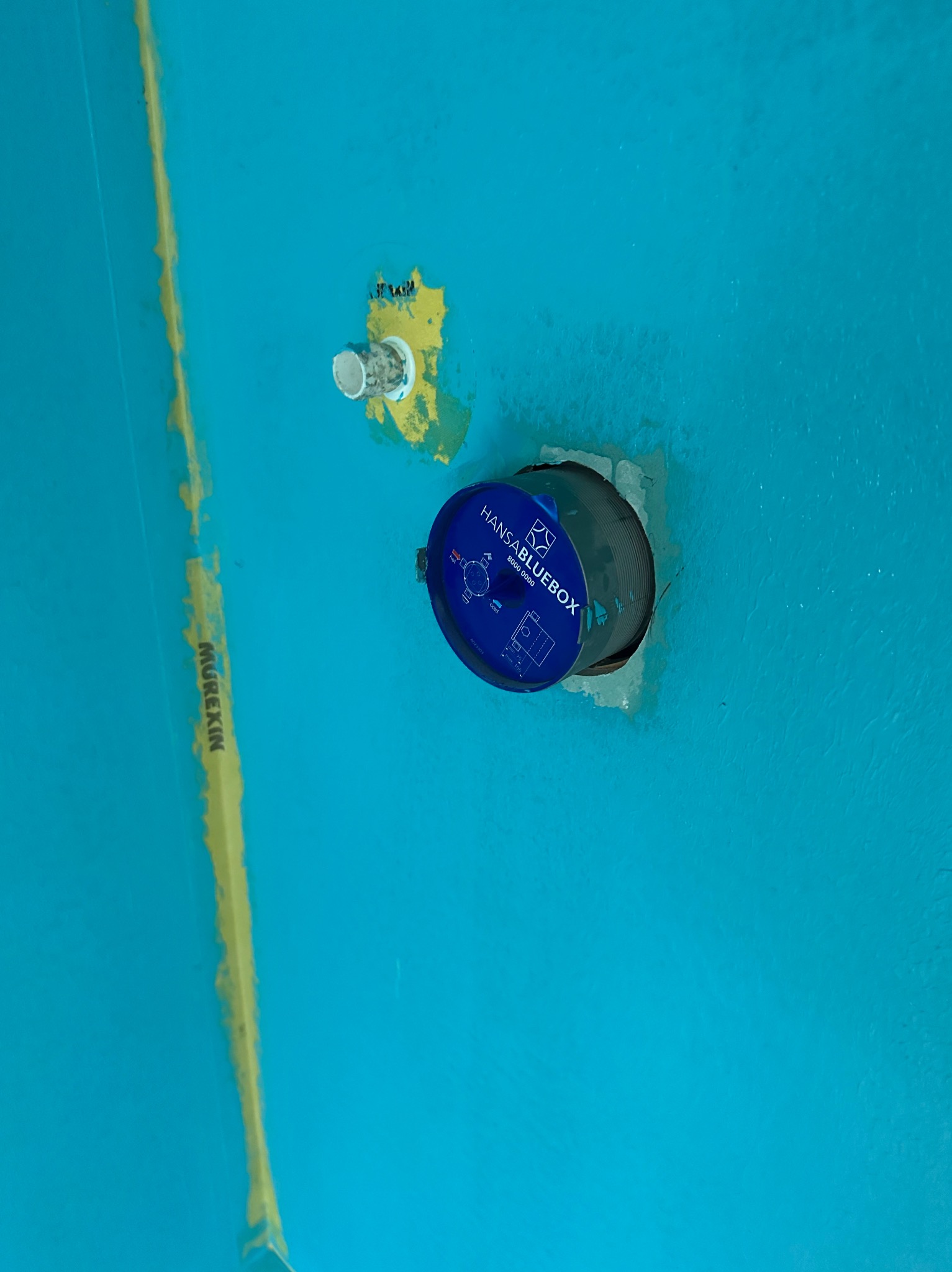 Niebieska ściana z zamontowaną podtynkową baterią Hansabluebox, widoczne ślady po wcześniejszych pracach i żółta linia Murexin na ścianie.