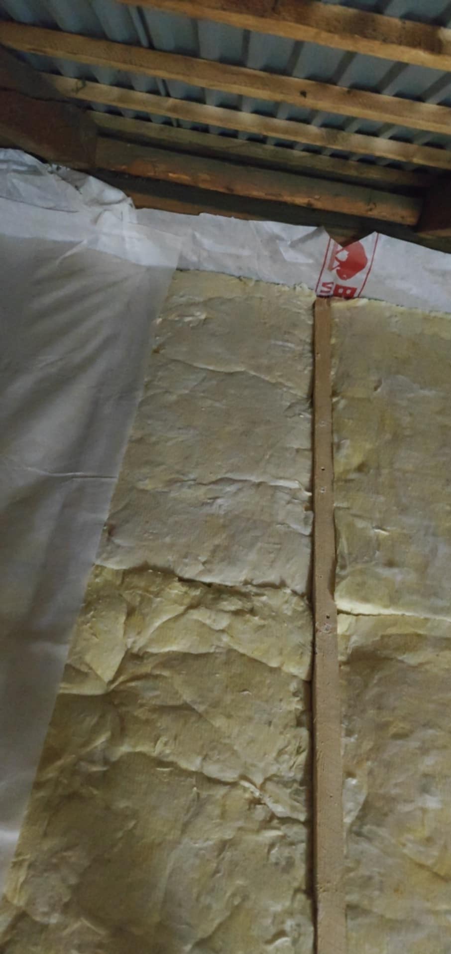 Ocieplenie poddasza wełną mineralną, zabezpieczone folią, Zakliczyn. Widoczna drewniana listwa mocująca. Prace wykończeniowe na poddaszu.