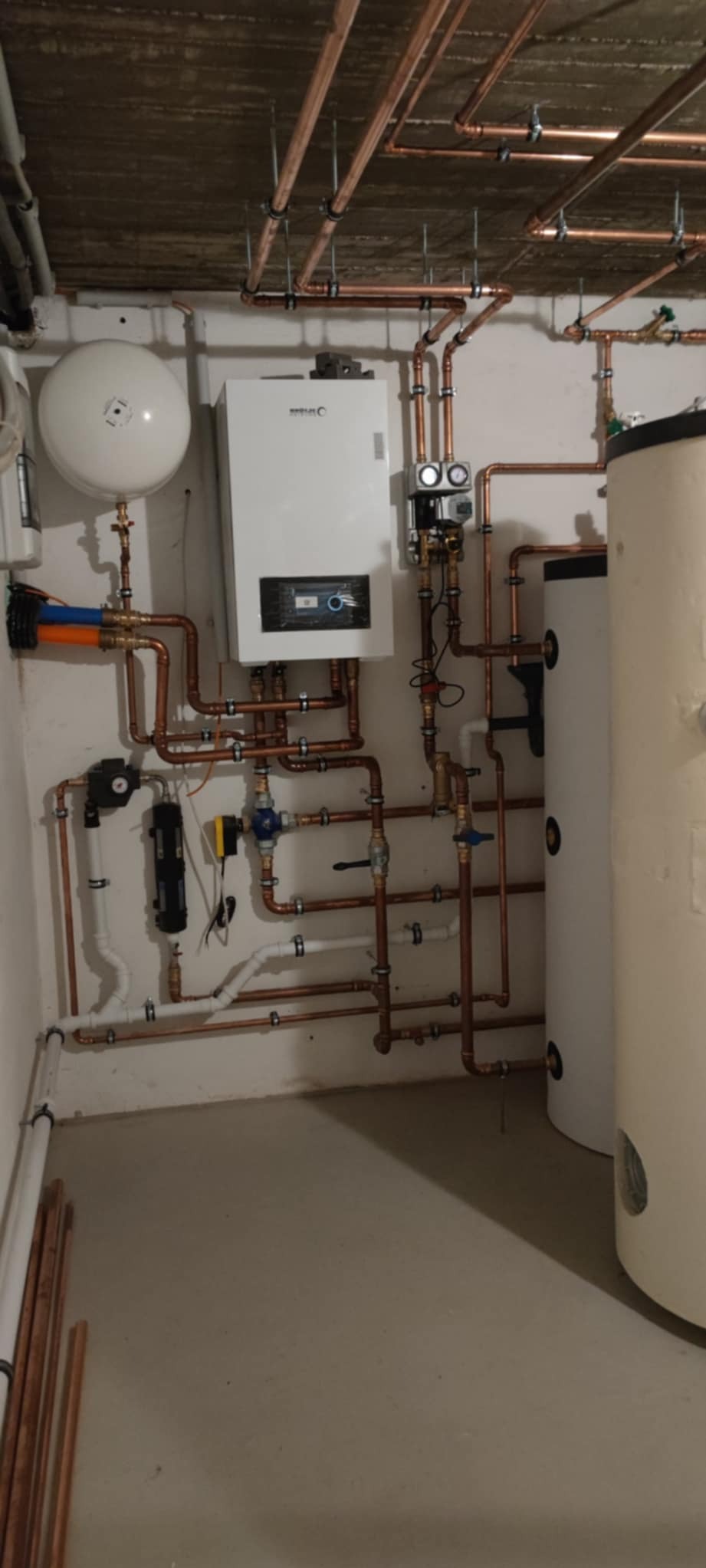 Kompleksowa instalacja grzewcza z miedzianymi rurami, zbiornikiem i kotłem w kotłowni. Widoczne liczne zawory i elementy montażowe.
