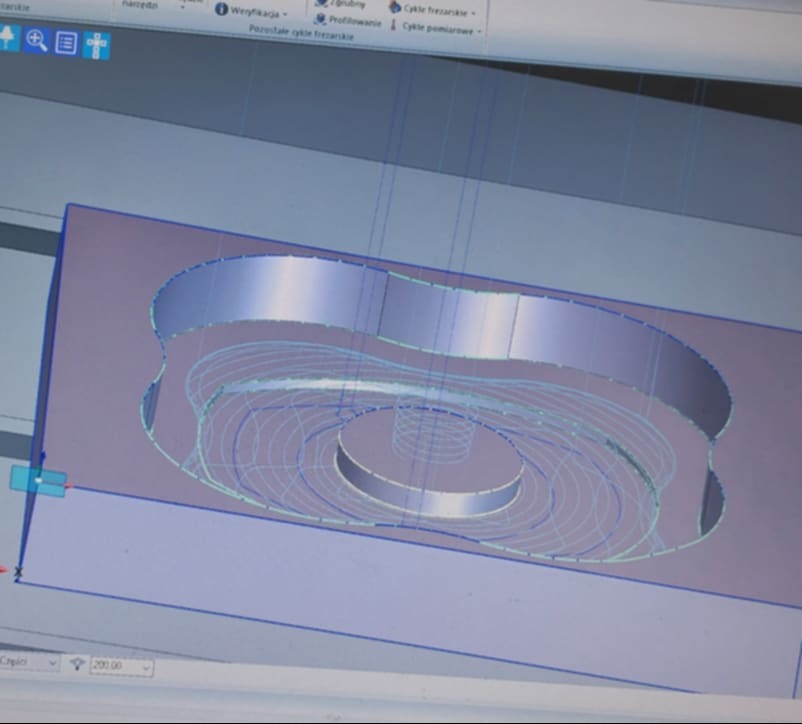 Ekran monitora prezentujący model 3D z widocznymi ścieżkami narzędzi frezarskich, prawdopodobnie w programie CAD/CAM, zarys obrabianego elementu w kolorze szarym.