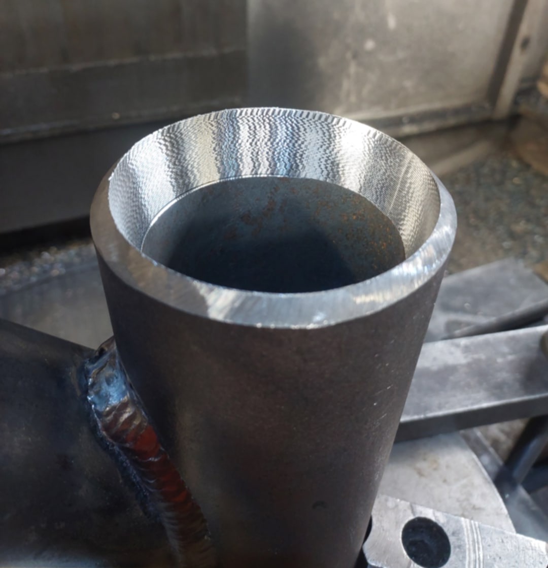 Metalowy element rurowy po obróbce, widoczne ślady frezowania na krawędzi, spawane połączenie. Detal z bliska, surowe wykończenie.