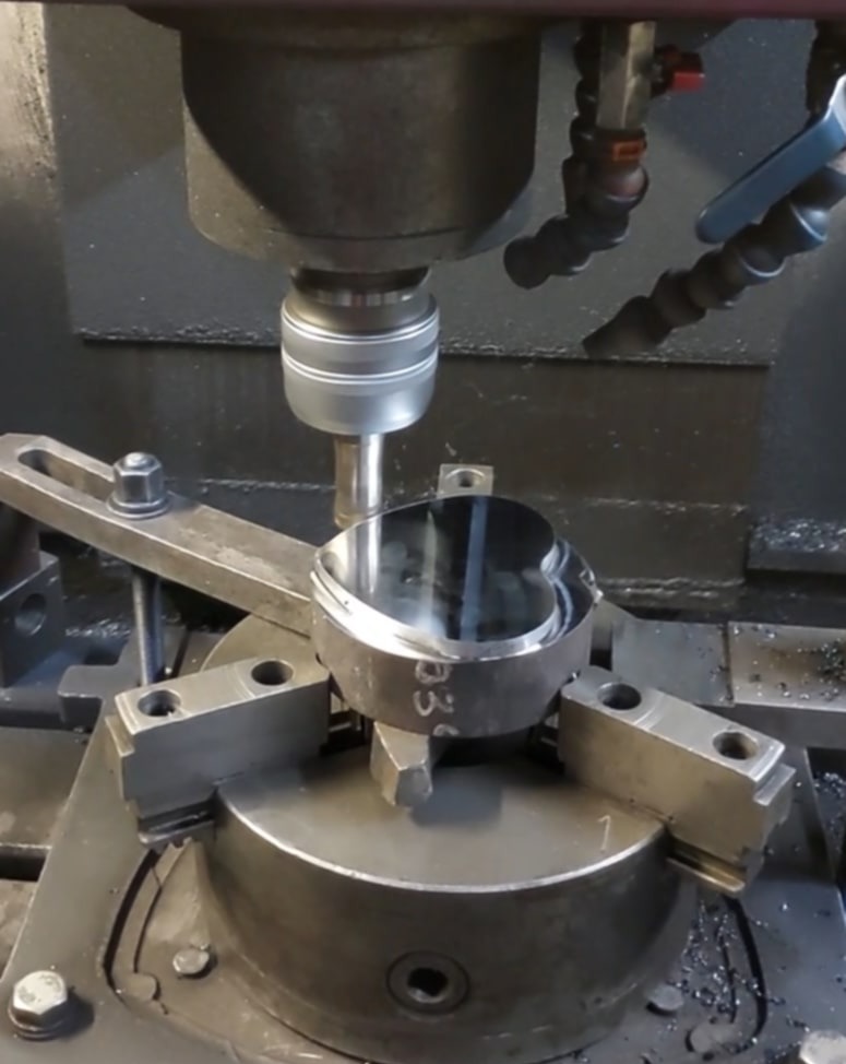 Precyzyjna obróbka metalu na tokarce CNC. Detal w uchwycie, wiertło w trakcie pracy, widoczne chłodziwo. Powierzchnia obrabianego elementu lustrzana.