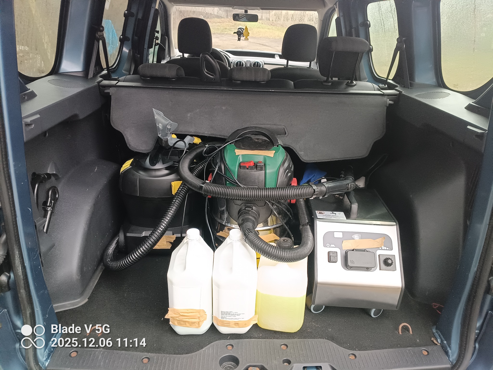 Wyposażenie do czyszczenia tapicerki w bagażniku auta w Sieradzu. Widoczne odkurzacze, pojemniki z płynami i parownica. Sprzęt gotowy do użycia.