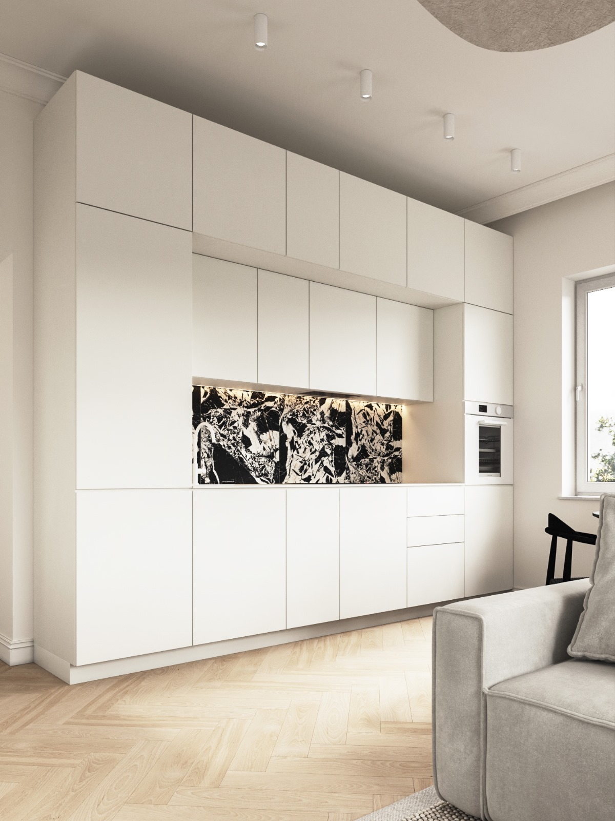 Nowoczesna, minimalistyczna kuchnia z białymi szafkami i czarnym marmurowym panelem nad blatem, oświetlonym od spodu. Parkiet w jodełkę i fragment sofy w tle.