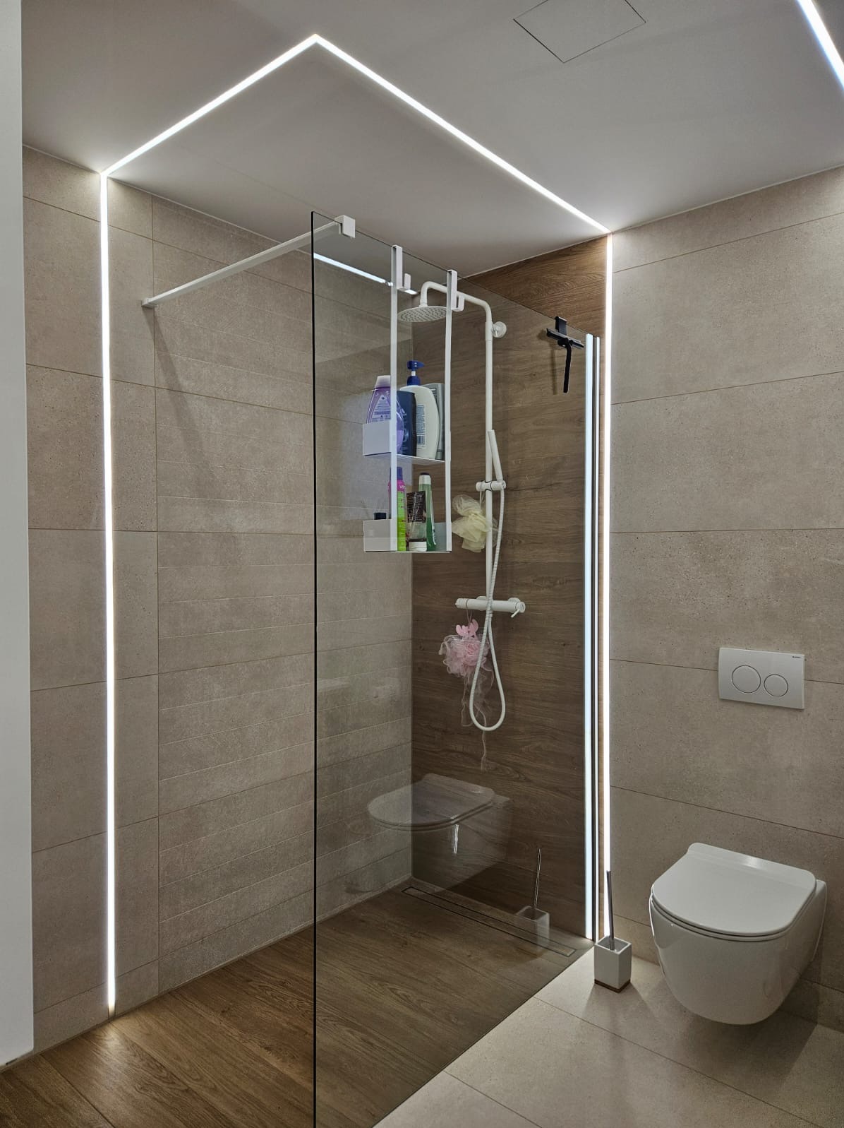 Nowoczesna łazienka z kabiną typu walk-in, podświetleniem LED wzdłuż ścian i sufitu, oraz drewnopodobną podłogą i ścianą w strefie prysznica. Minimalistyczny design.