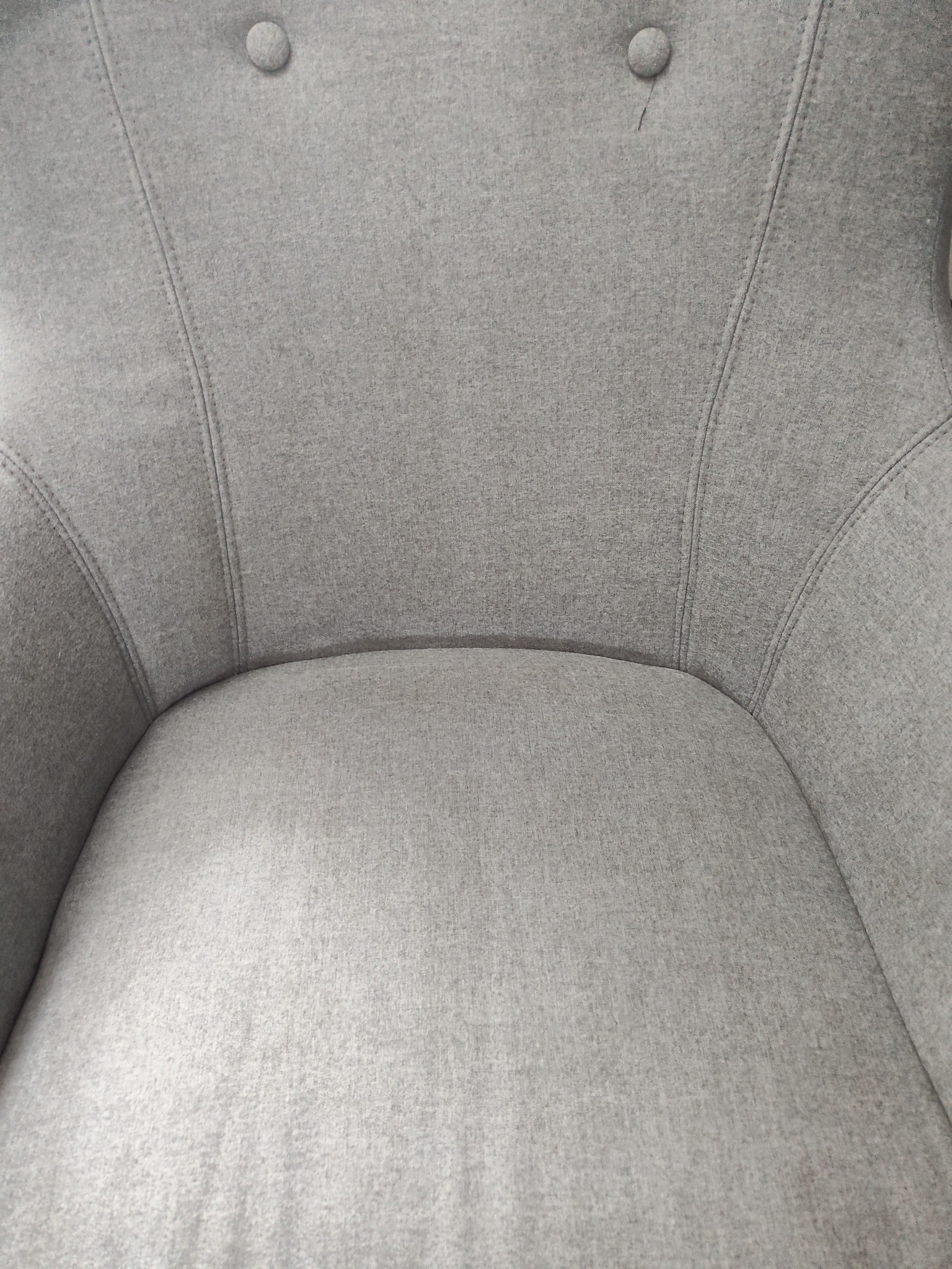 Szczegółowe ujęcie szarego fotela tapicerowanego z dwoma guzikami, prezentujące fakturę materiału i precyzyjne szwy. Widok z góry na siedzisko i oparcie.