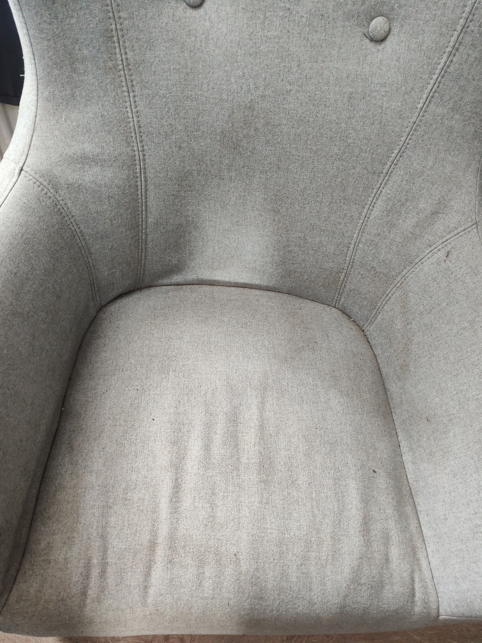 Szare, tapicerowane krzesło z widocznymi zabrudzeniami na siedzisku i oparciu, ukazujące potrzebę odświeżenia tapicerki.