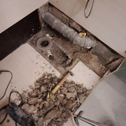 Rem-Bud Waw - Demontaż starej instalacji wodno-kanalizacyjnej w łazience podczas remontu. Widoczne narzędzia, gruz i fragment kabiny prysznicowej.