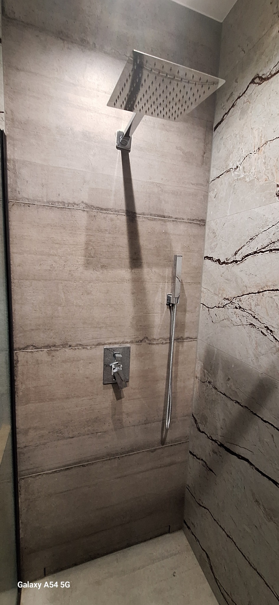 Nowoczesna kabina prysznicowa z deszczownicą i baterią podtynkową, wykończona płytkami imitującymi drewno i marmur. Minimalistyczny design.