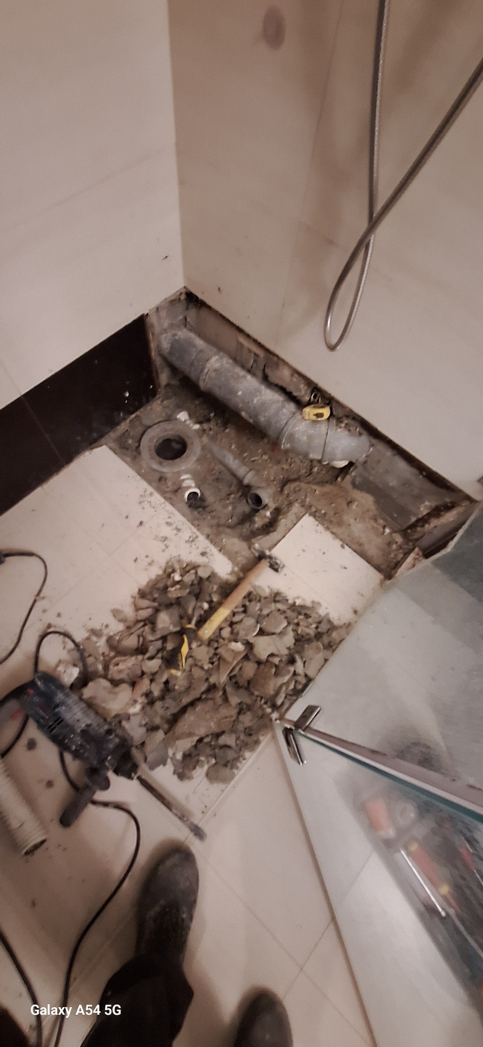 Demontaż starej instalacji wodno-kanalizacyjnej w łazience podczas remontu. Widoczne narzędzia, gruz i fragment kabiny prysznicowej.