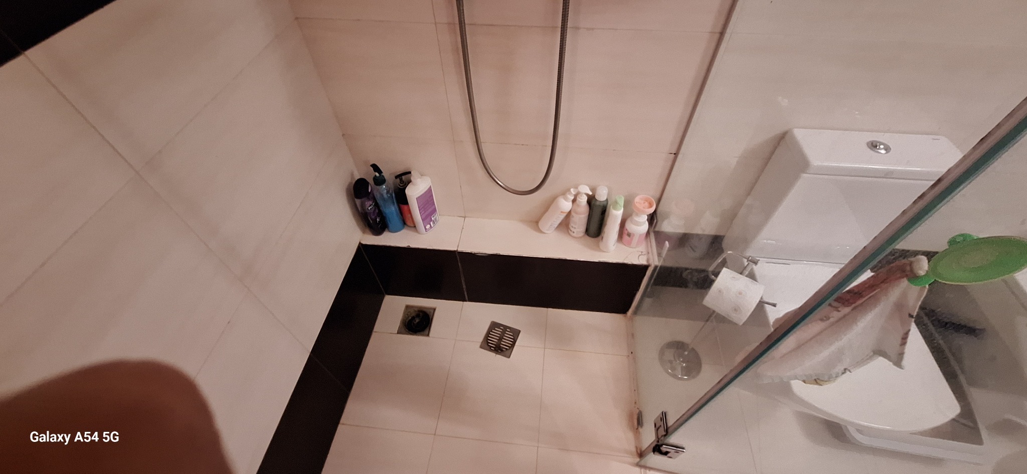 Wykończona łazienka w Warszawie z kabiną prysznicową, toaletą i białymi płytkami. Widoczne kosmetyki i akcesoria łazienkowe. Ujęcie z góry.