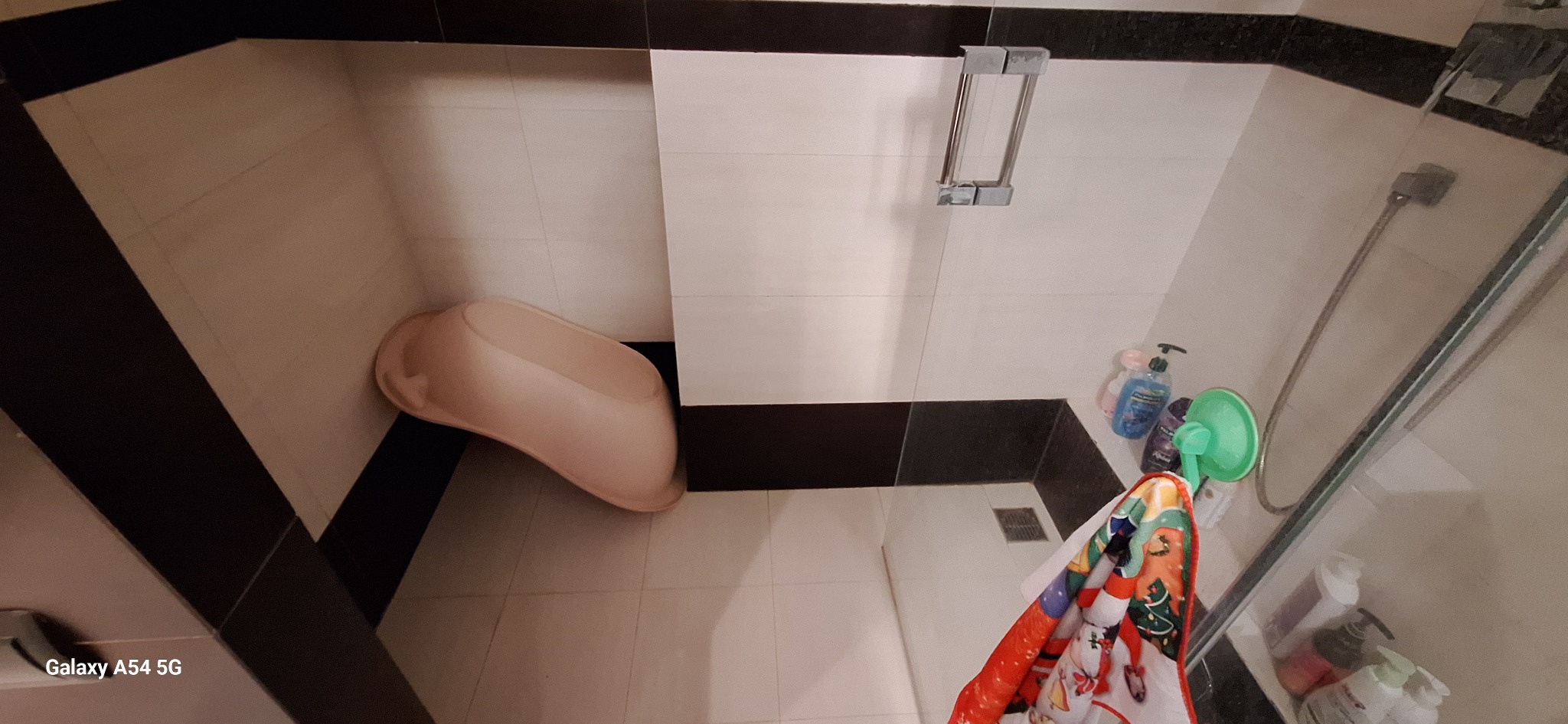 Wykończona łazienka z biało-czarnymi płytkami, widoczna wanna dla dziecka, kabina prysznicowa i akcesoria łazienkowe. Ujęcie z góry.