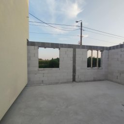 Radbud - Wnętrze surowego domu w trakcie budowy: ściany z betonu komórkowego z otworami okiennymi, w tle zieleń. Widoczne ślady zaprawy. Stan surowy zamknięty.