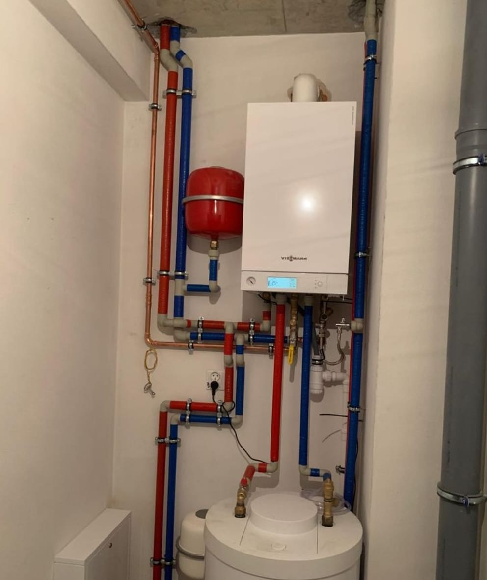 Biały piec gazowy Viessmann z czerwonym zbiornikiem wyrównawczym i instalacją z rur miedzianych i plastikowych w kolorach niebieskim i czerwonym, zamontowany w kotłowni.