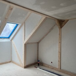 EU INVEST Daniel Krotochwil - Poddasze w trakcie remontu: drewniana konstrukcja, okna dachowe zabezpieczone folią, ściany przygotowane do malowania, surowa żarówka. Widoczne materiały budowlane.