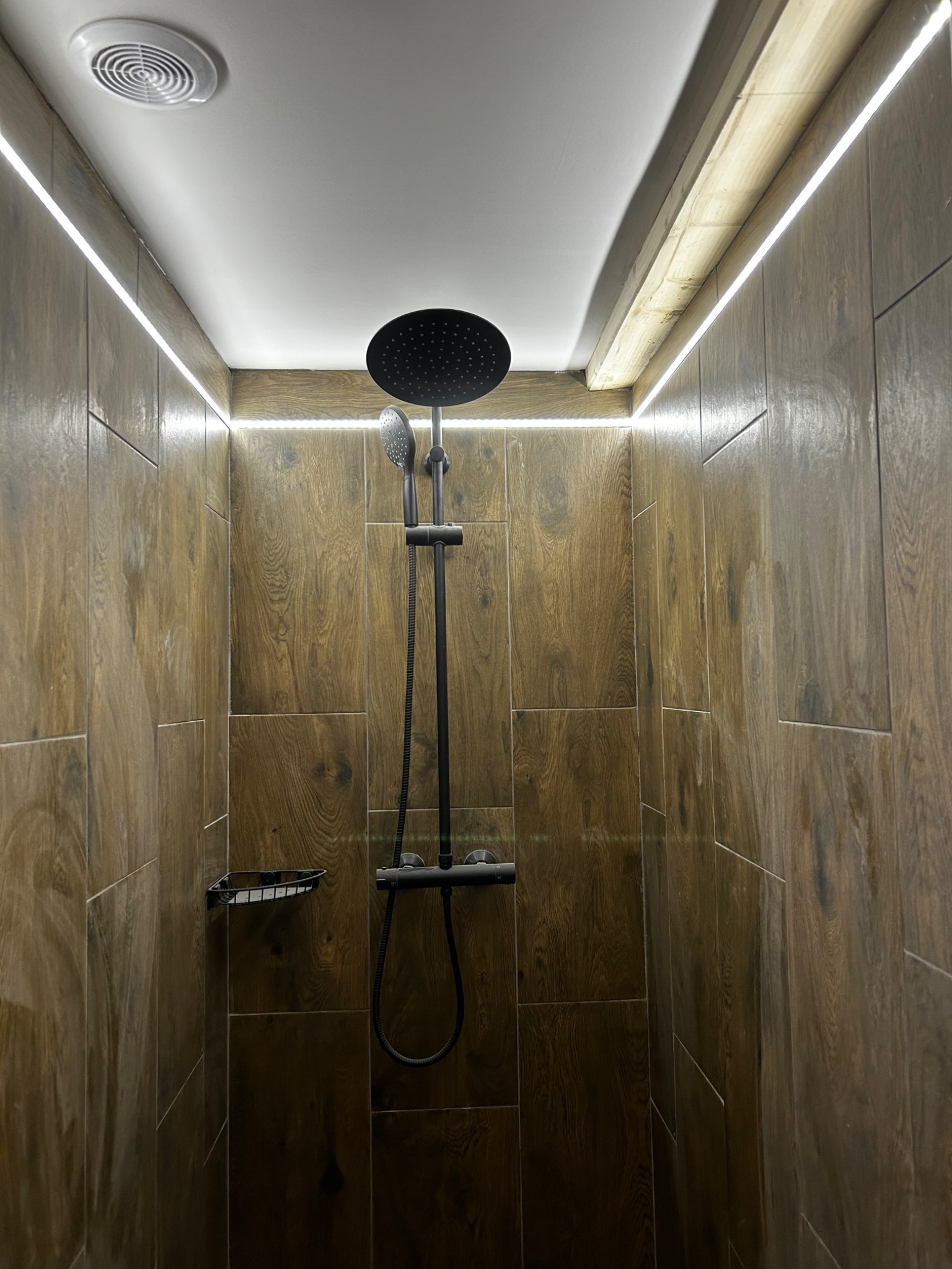 Nowoczesna kabina prysznicowa z deszczownicą i panelami imitującymi drewno, oświetlona listwami LED, tworzącymi ciepły klimat.