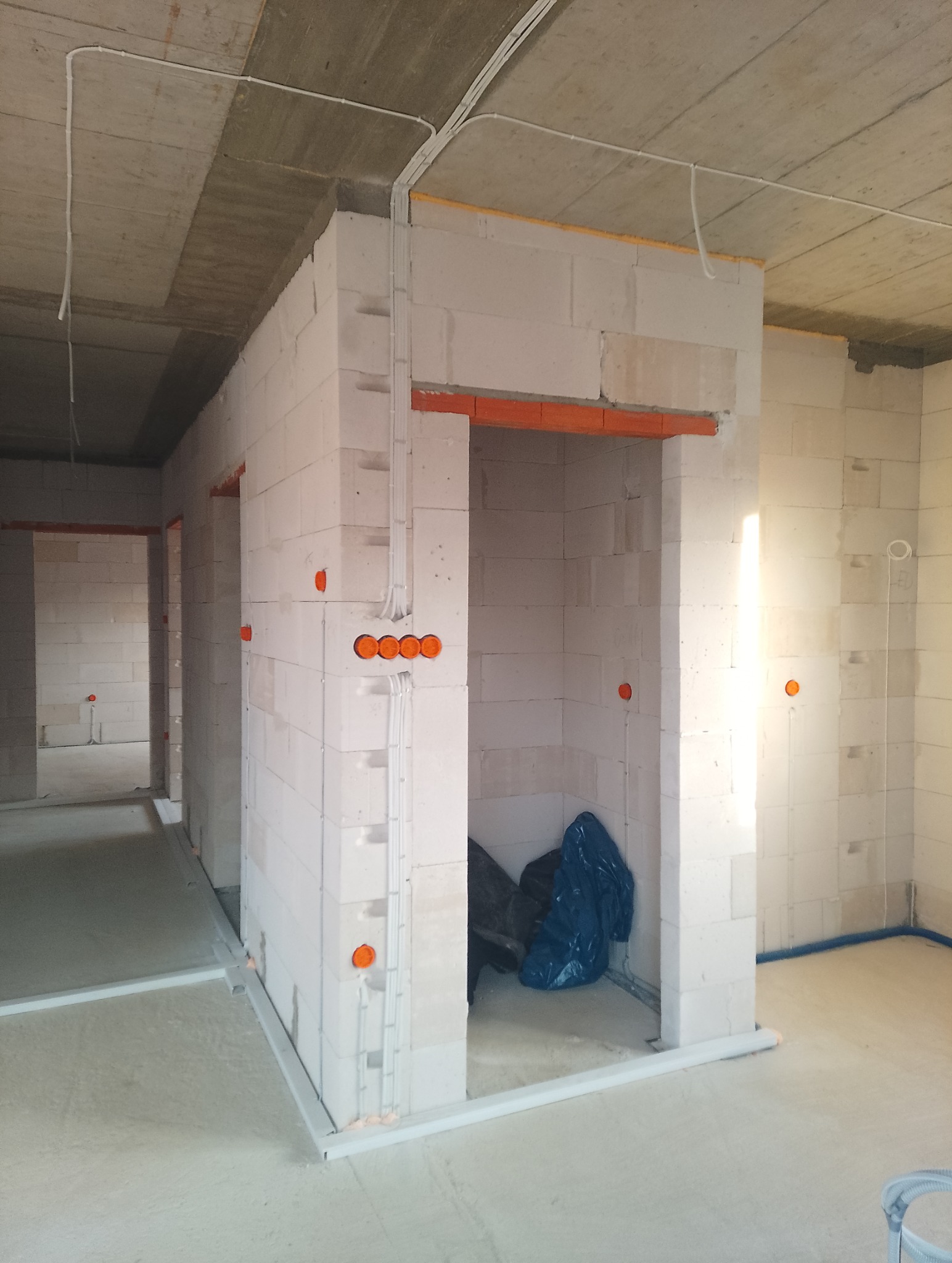 Surowy stan: instalacja elektryczna w budynku z białych bloczków, widoczne kable, puszki i rury instalacyjne. Pomieszczenie w trakcie wykończenia.