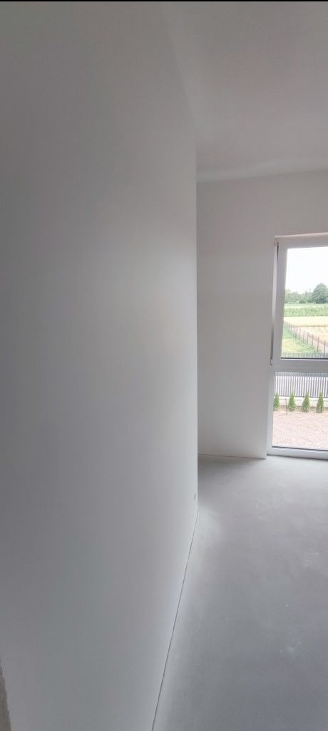 Wnętrze po malowaniu na biało, widok na ścianę i okno z widokiem na zieleń. Minimalistyczny styl, świeżo pomalowane ściany i podłoga.