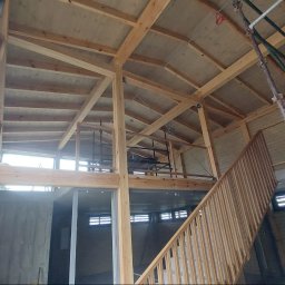 Sneker - Wnętrze domu szkieletowego w trakcie budowy: drewniana konstrukcja, schody, okna. Widoczne rusztowania i elementy wykończeniowe.