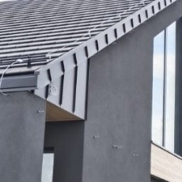 Sneker - Nowoczesny dom z ciemną elewacją i dachem z blachy trapezowej, widok z dołu, podkreślający geometrię budynku i minimalistyczny design.