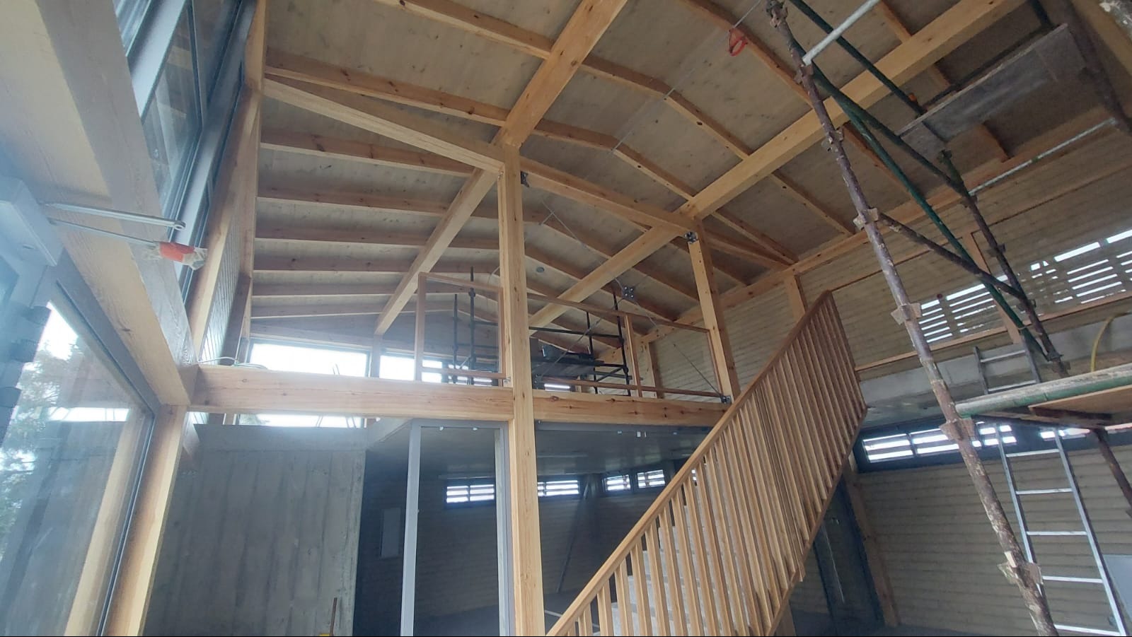 Wnętrze domu szkieletowego w trakcie budowy: drewniana konstrukcja, schody, okna. Widoczne rusztowania i elementy wykończeniowe.