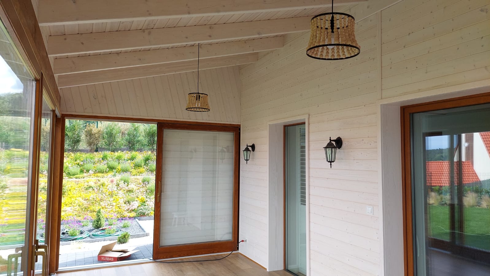 Jasne, drewniane wnętrze z dużymi oknami przesuwnymi, przez które widać kwitnący ogród. Dwa ozdobne żyrandole i kinkiety dodają przytulnego charakteru.