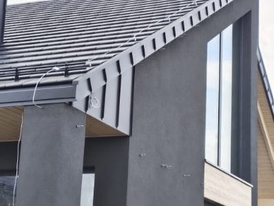 Nowoczesny dom z ciemną elewacją i dachem z blachy trapezowej, widok z dołu, podkreślający geometrię budynku i minimalistyczny design.