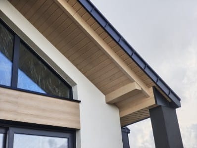 Nowoczesny dom z drewnianą podbitką dachową i czarnymi obróbkami blacharskimi, widok z dołu, akcent na detale wykończenia.