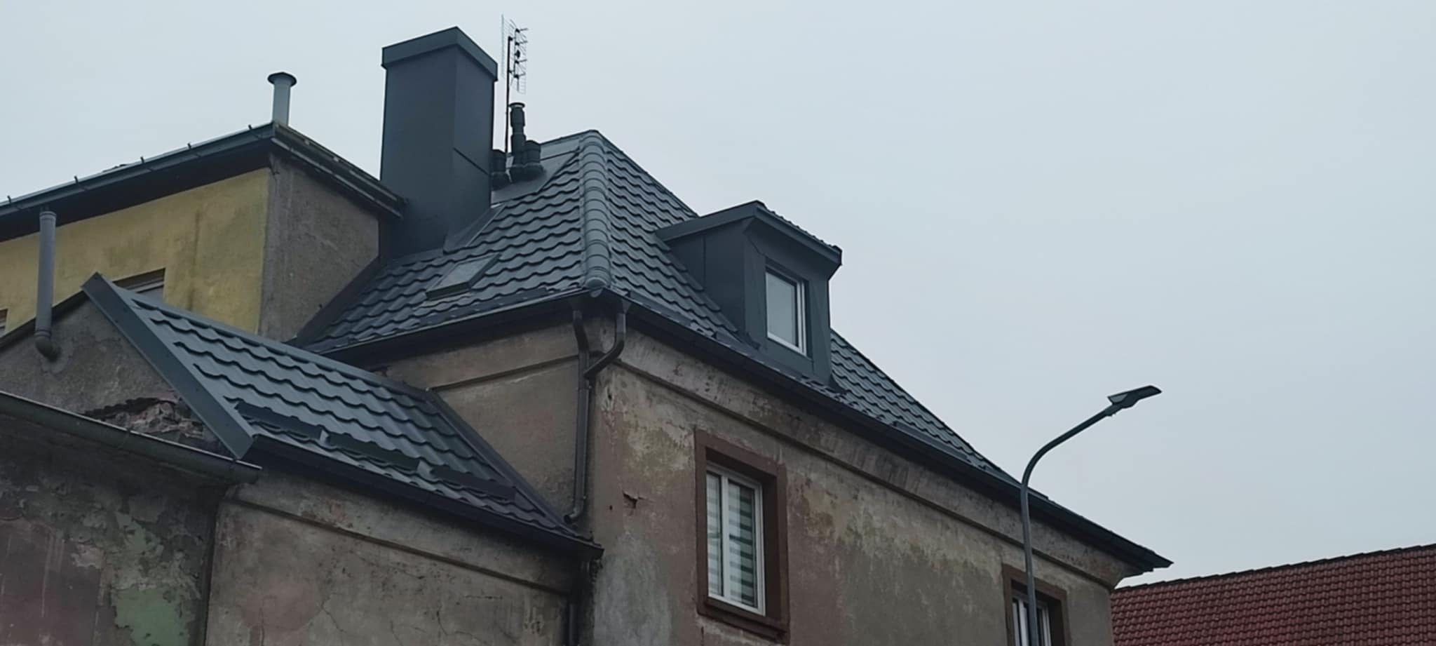 Odnowiony dach z blachy trapezowej na kamienicy w Drawsku Pomorskim, z nowymi obróbkami blacharskimi i kominem. Widoczne okno dachowe i rynny.