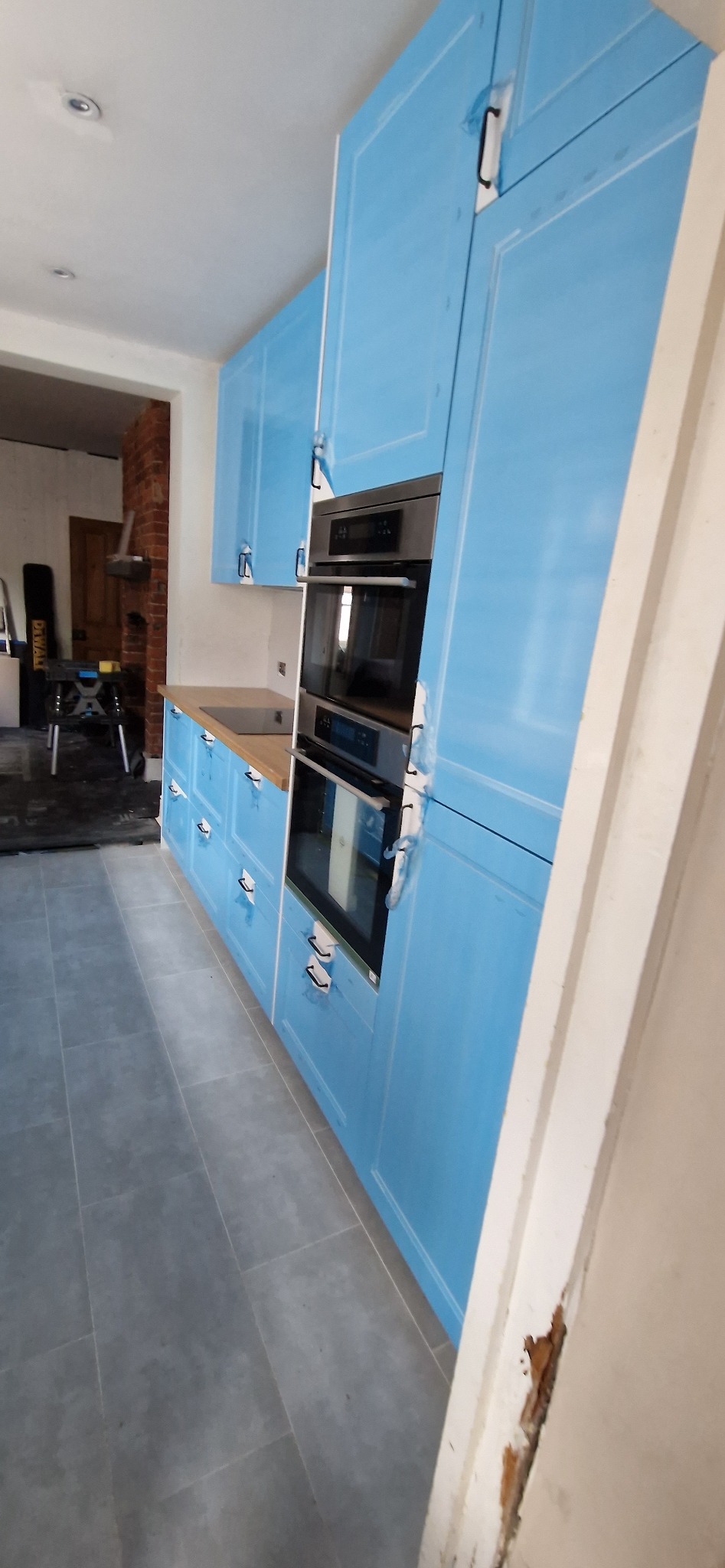 Błękitna zabudowa kuchenna z piekarnikiem w Łodzi, jeszcze z folią ochronną, na tle szarych płytek podłogowych i fragmentu remontowanego pomieszczenia.