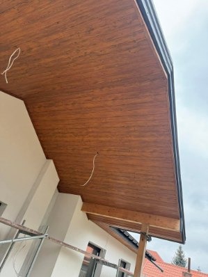 Drewniana podbitka dachowa z widocznymi elementami konstrukcyjnymi i fragmentem rusztowania. Ujęcie z dołu, podkreślające strukturę drewna i detale wykończenia.