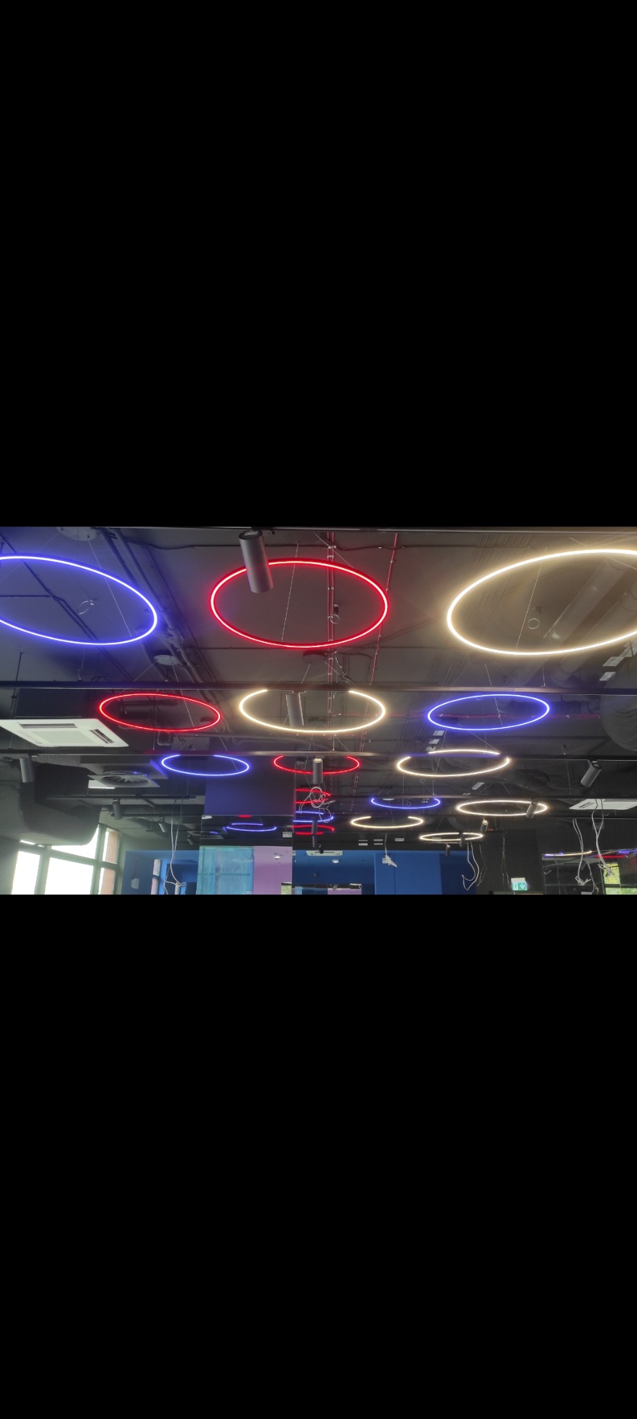 Nowoczesne oświetlenie sufitowe z okrągłych lamp LED w kolorach: niebieskim, czerwonym i białym. Widoczne elementy instalacji i wentylacji.