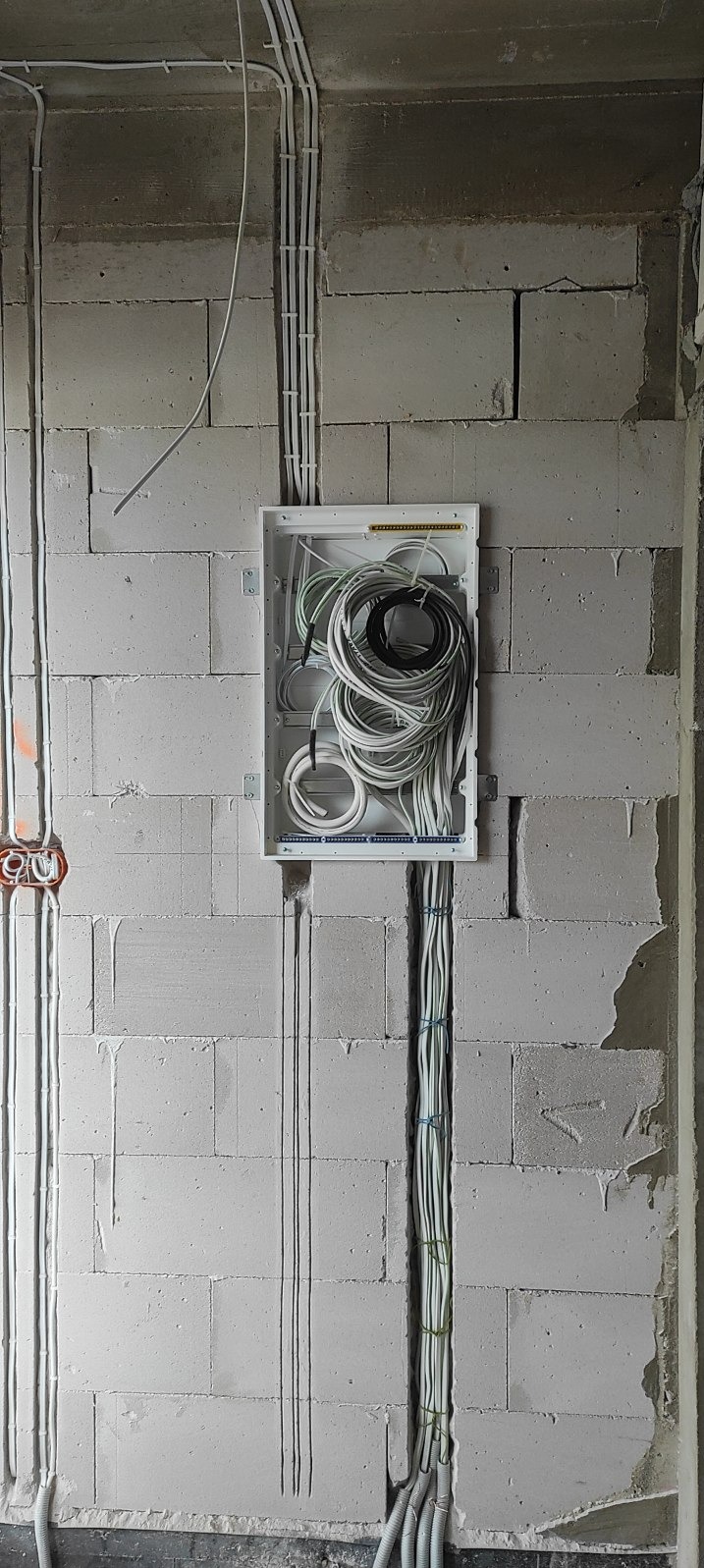 Rozdzielnica elektryczna z poprowadzonymi przewodami w ścianie z betonu komórkowego. Instalacja w trakcie montażu, widoczne kable i peszle.