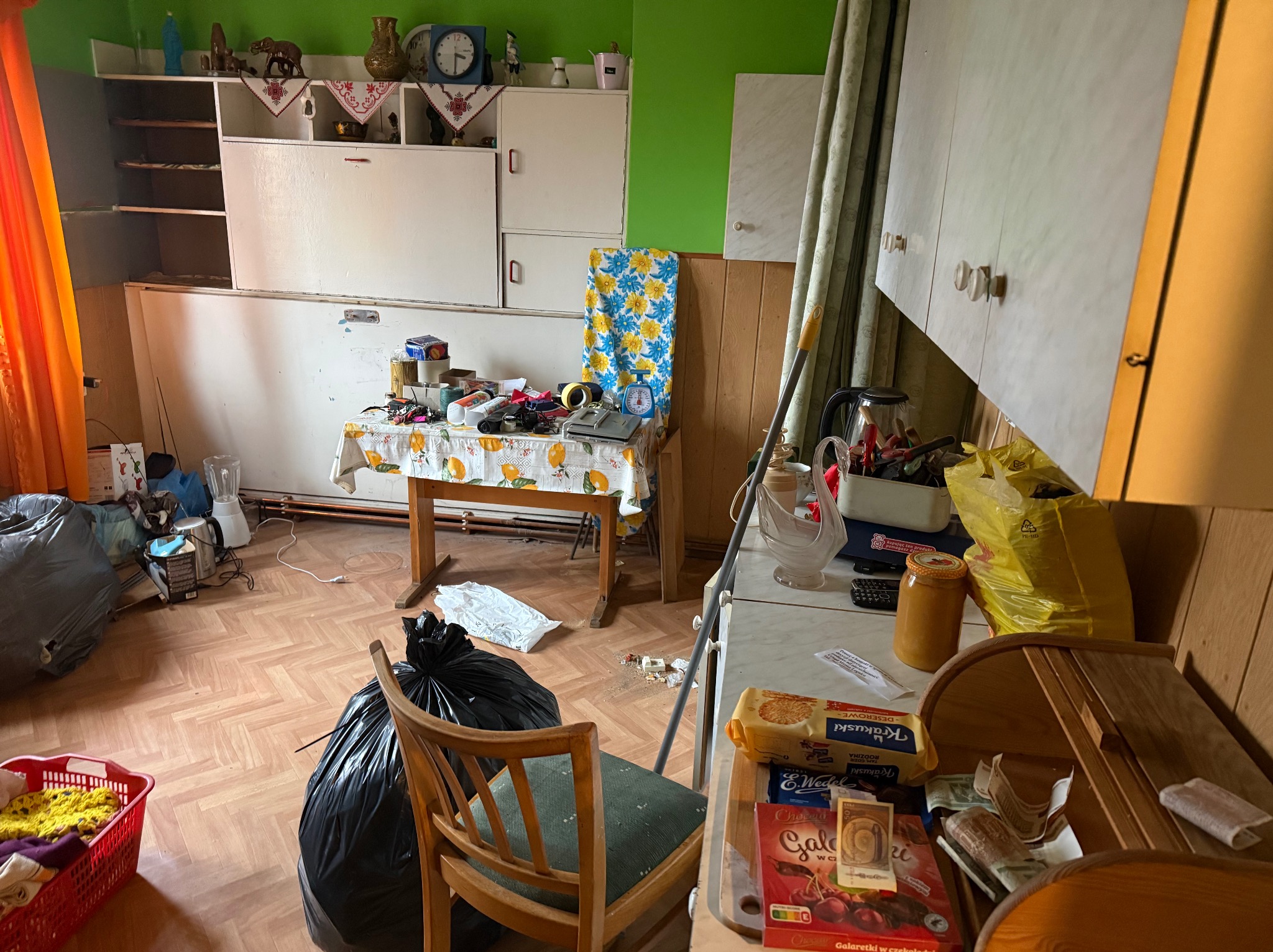 Zagracona kuchnia przed opróżnianiem: worki na śmieci, stare meble, resztki jedzenia. Widok na bałagan przed sprzątaniem i wywozem.
