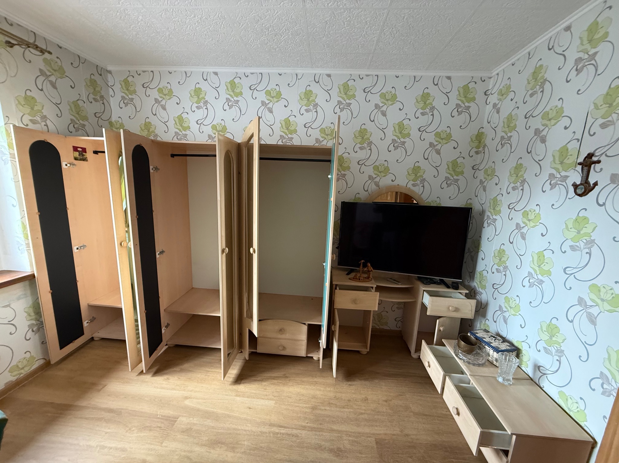 Demontaż mebli: rozłożona szafa z lustrami i komoda w pokoju z tapetą w kwiaty. Przygotowanie do przeprowadzki lub opróżniania mieszkania.